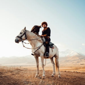 Person in traditional clothing riding white horse with eagle.
